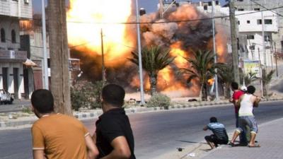 Palestinian men look on as a bomb from an Israeli air strike hits a house in Gaza City on August 23, 2014