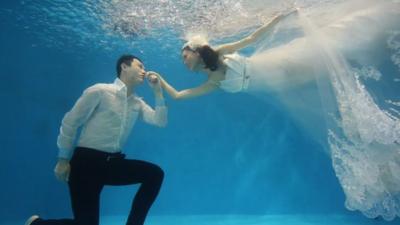 A groom kissing his bride's hand in an underwater photo shoot