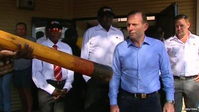 Tony Abbott watches a man play a didgeridoo as he arrives in northeast Arnhem Land