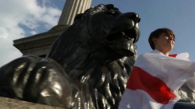 Girl wrapped in England flag sitting in front of lion statue in London's Trafalgar Square