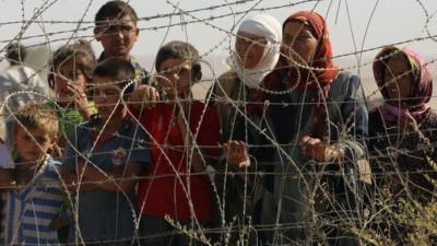 Refugees standing behind barbed wire