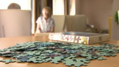 Jigsaw on table in foreground with older people out of focus in the background