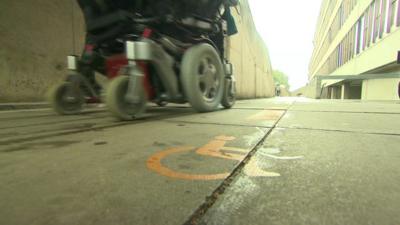 Person in an electric wheelchair going past a disabled sign on the ground