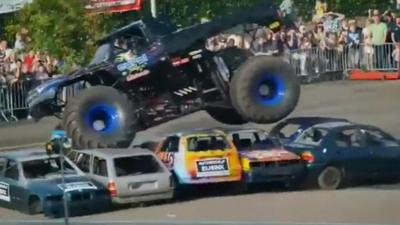 Monster truck driving over several empty cars