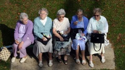 Five pensioners sat on park bench eating lunch