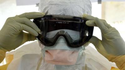 A health workers in protective suit puts glasses on