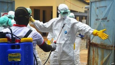 Health workers wearing protective suits prepare to carry the body of a victim of Ebola