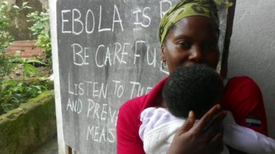 Woman and child in front of a blackboard with Ebola health