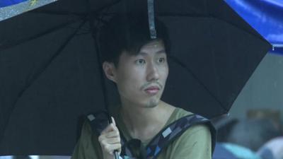 Hong Kong protester watching rain from under large umbrella