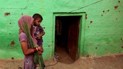 An Indian villager carries a child past a house where four members of a family were reported to have been killed in cross-border firing between Indian and Pakistani soldiers at Mashe de Kothe village in Arnia sector near the India-Pakistan border