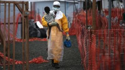 A Doctors Without Borders (MSF) health worker in protective clothing carries a child suspected of having Ebola in the MSF treatment centre in Paynesville, Liberia, 5 October 2014