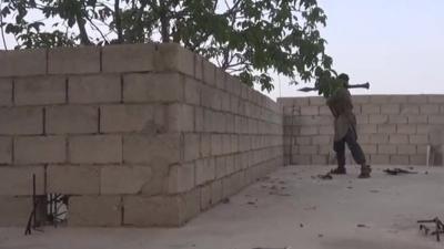 Islamic State fighter firing an RPG from behind a wall