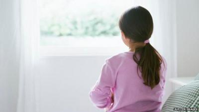 Young girl sitting alone on a bed.