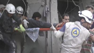 Workers in hard hats pull an injured man from a building.