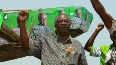 Michael Sata at a rally with his right fist raised in the air