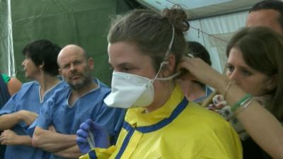 A healthcare worker being dressed in a protective suit