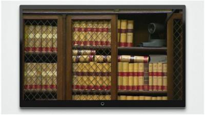 Television screen shows camera nestled amongst books on a shelf within the Royal Courts of Justice