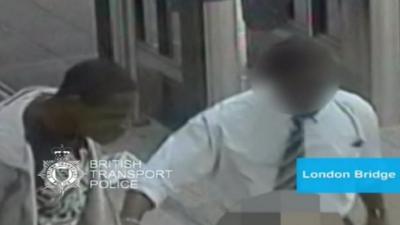 CCTV shot of the alleged attacker on the left next to a member of station staff (face blurred out)