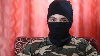 A 13-year-old boy who wishes to be named "Abu Hattab" sits wearing a black balaclava