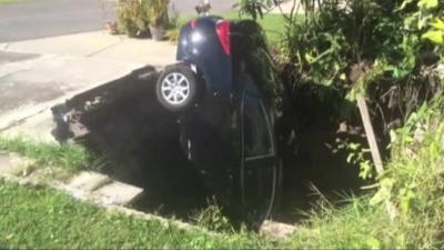 A car lies vertically after falling down into a sinkhole