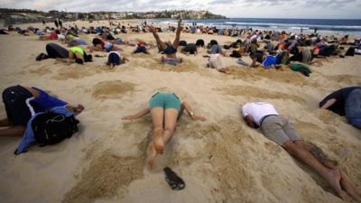 A group of around 400 demonstrators participate in a protest by burying their heads in the sand at Sydney's Bondi Beach