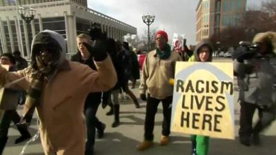 Protesters in St Louis including one with a placard reading 'Racism lives here' written on top of a picture of the Gateway Arch