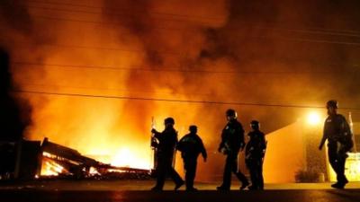 Police in riot gear walk past a burning building in Ferguson, Missouri