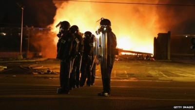 Police officers watch as a business burns after it was set on fire during rioting