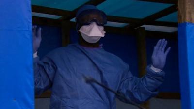 A health worker in hazmat suit being sprayed
