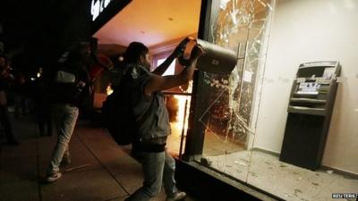 A demonstrator breaks the window of an ATM machine