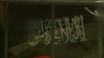 A black flag bearing the white Arabic text of the "shahada", the basic statement of the Islamic faith, being held in the Lindt Chocolat Cafe, Sydney, 15 December 2012