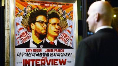 A security guard stands near a poster for The Interview