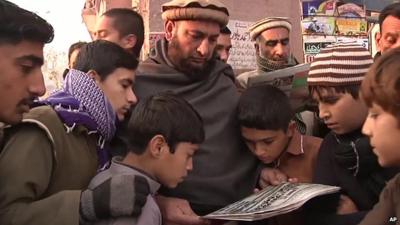 Two men and a group of children in Peshawar, Pakistan, gathered together to look at a newspaper reporting Taliban school attack