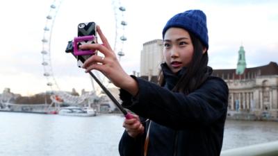 A young woman takes self-portrait with a selfie stick in central London