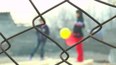 Girls playing with balloons behind barbed wire