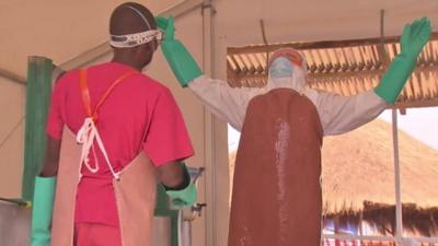 Ebola health worker sprays disinfectant on a colleague in protective gear at a Save the Children Ebola treatment centre in Kerry Town Sierra Leone