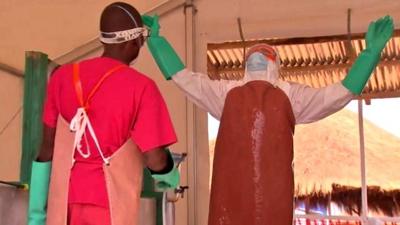 Ebola health worker sprays disinfectant on a colleague in protective gear at a Save the Children Ebola treatment centre in Kerry Town Sierra Leone