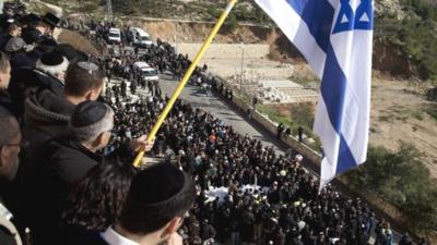 Mourners hold an Israeli flag while standing on a wall during the Jerusalem funeral of four men killed in an attack on a kosher supermarket in Paris