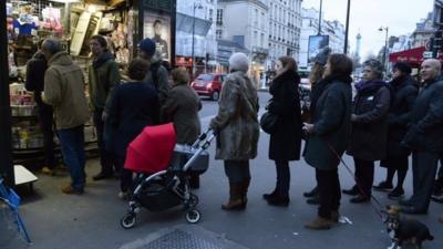 People wait outside a newsagents kiosk in Paris