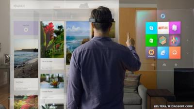 Publicity photo showing model wearing Microsoft HoloLens and scrolling through virtual Windows menu