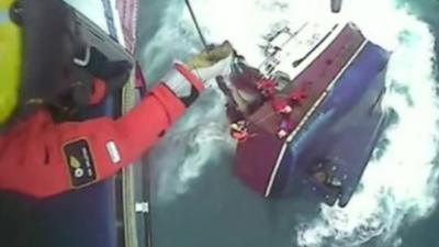 A rescue worker lowers a line to the fishermen as their boat sinks