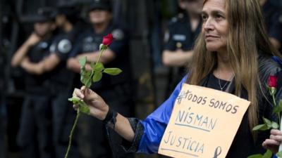 A woman holding roses wears a sign that reads in Spanish "We"re all Nisman. Justice" near the funeral home where a private wake is held for prosecutor Alberto Nisman in Buenos Aires