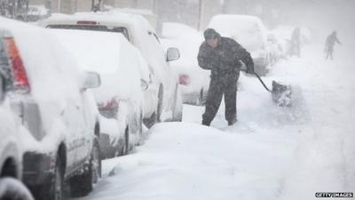 A man digs out his car along a snow-covered street