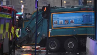 Emergency service trucks are parked near a bin lorry at the scene of the crash