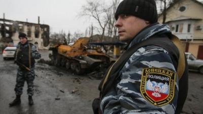 Members of the police of the separatist self-proclaimed Donetsk People"s Republic gather near a burnt-out armoured vehicle in Vuhlehirsk, Donetsk region