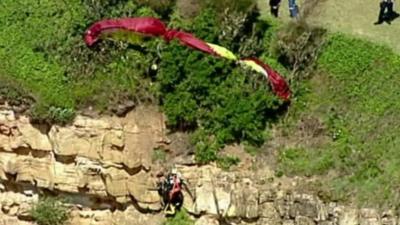 The paraglider can be seen dangling from the rock face