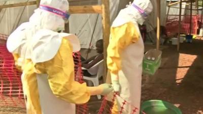 Two aid workers clad in protective clothing enter a tent in Sierra Leone.