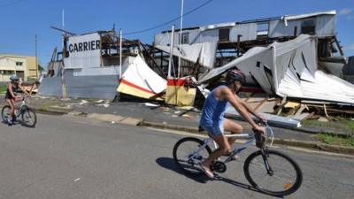 Residents cycle past a cyclone damaged business in the northern Queensland town of Rockhampton