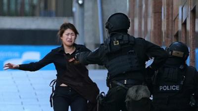 Bae Jie-un, a staff member of a Sydney cafe and one of the hostages, runs to armed tactical response police officers for safety after she escaped from a cafe under siege in Sydney