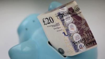 A £20 note placed in top of a piggy bank
